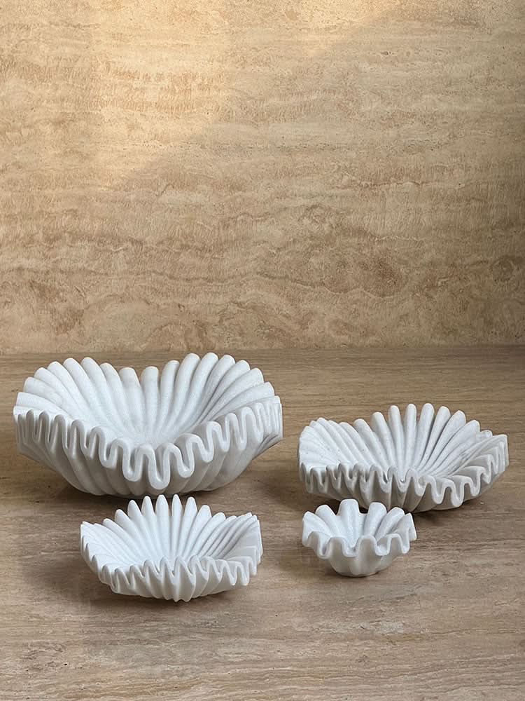 White fluted marble fruit bowls on a textured beige surface.
